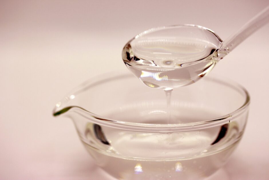 ガラスの器に入った透明の油を、ガラススプーンですくって垂らしている様子
