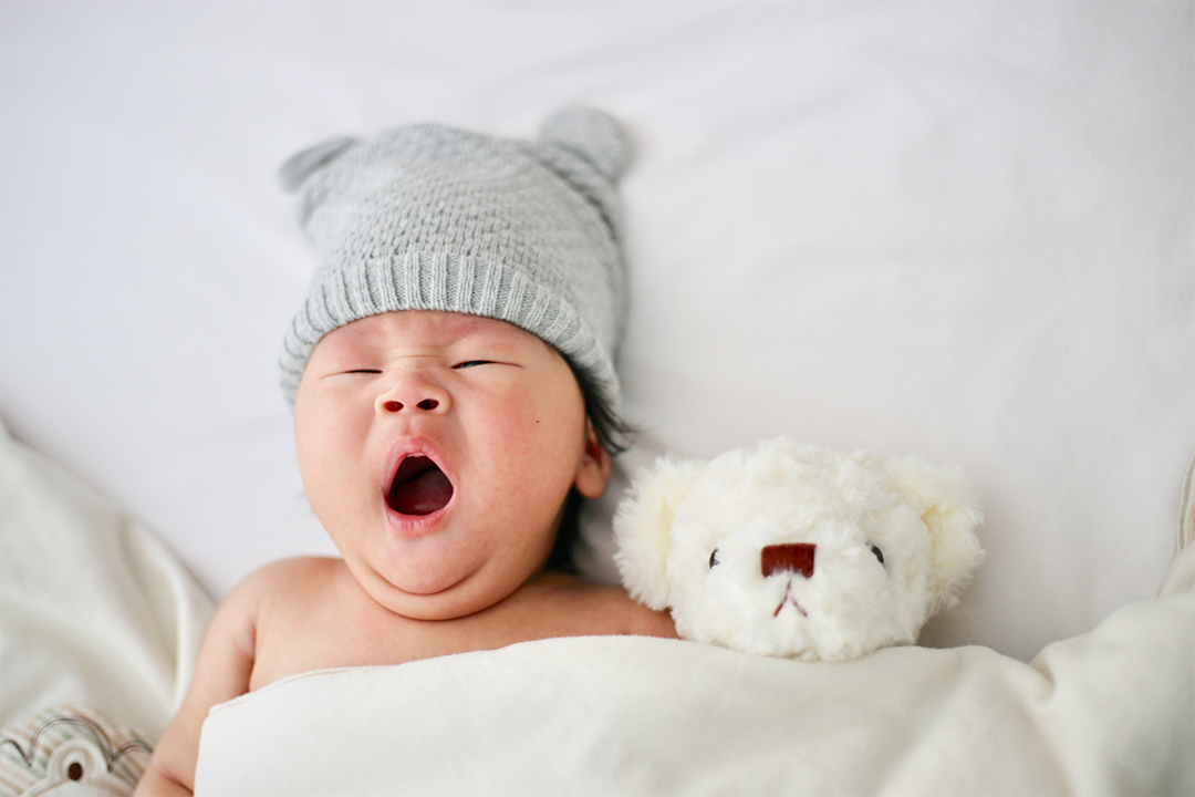 あくびをしている帽子を被った赤ちゃんと白くまのぬいぐるみ